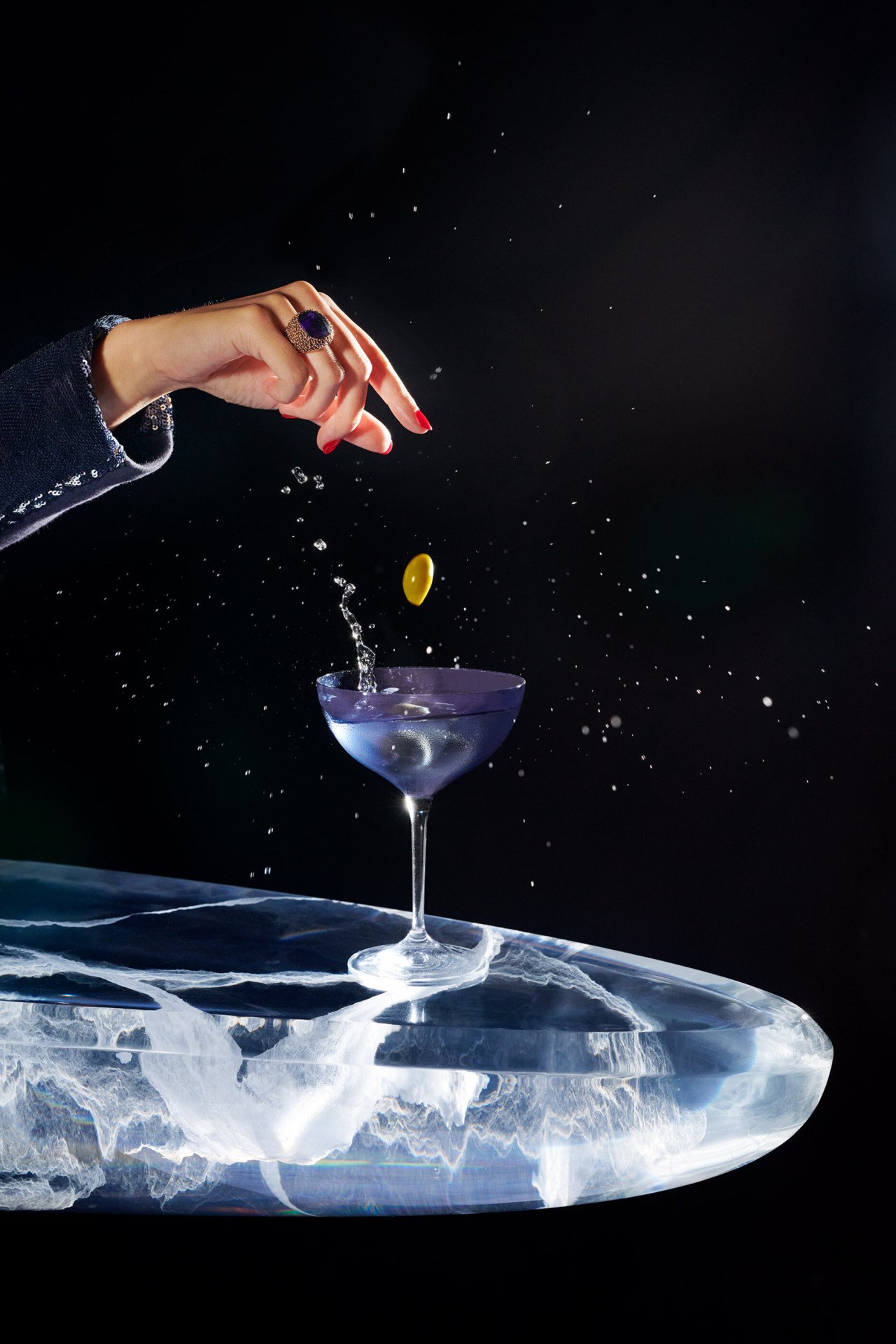 dry martini cocktail on a black backdrop with a hand dropping olives