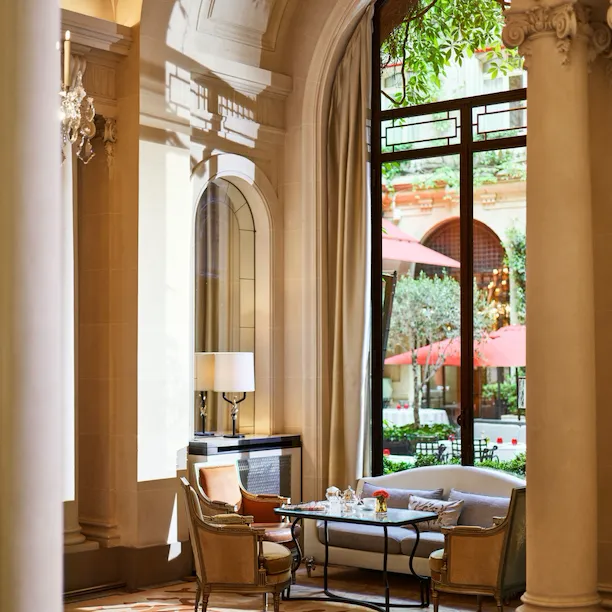 Dining table at la galerie, table with cups of tea, two armchairs and a sofa next to a sunny window giving on the Cour Jardin Courtyard, at Hotel Plaza Athénée, Paris