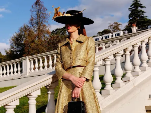 A person in a hat and gold skit standing on the stairs that lead from the croquet lawn to the rose garden in the Grounds of Coworth Park