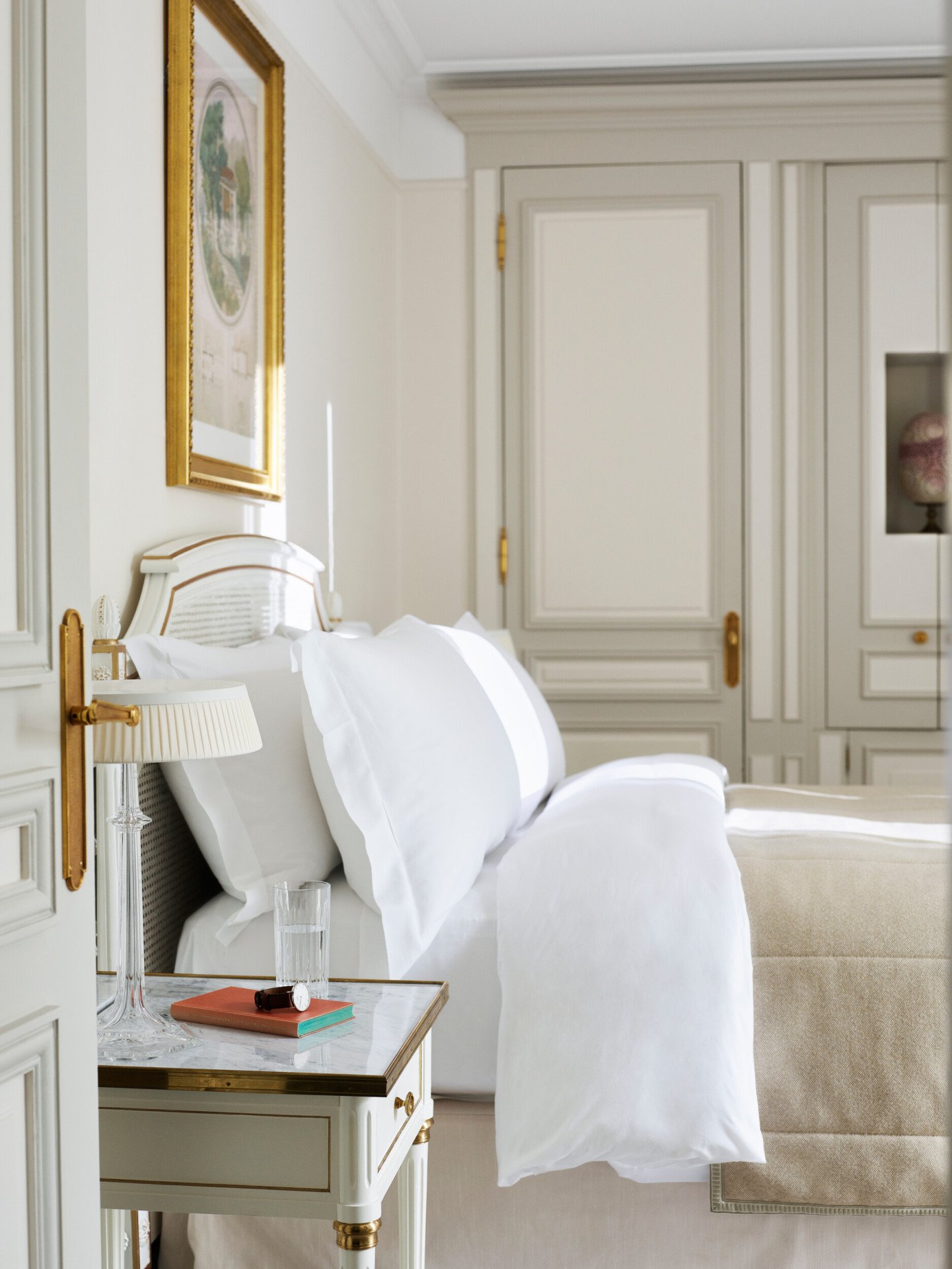 Bedroom in beige and white shades with a wooden closet in the background and a queen bed. At Le Meurice, Paris.
