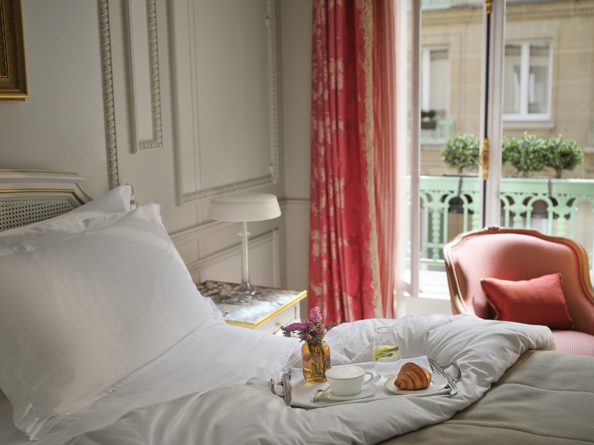 Plan on the top of the bed with a breakfast tray on it, with a cup of coffee, a croissant and a flower arrangement , at Le Meurice, Paris