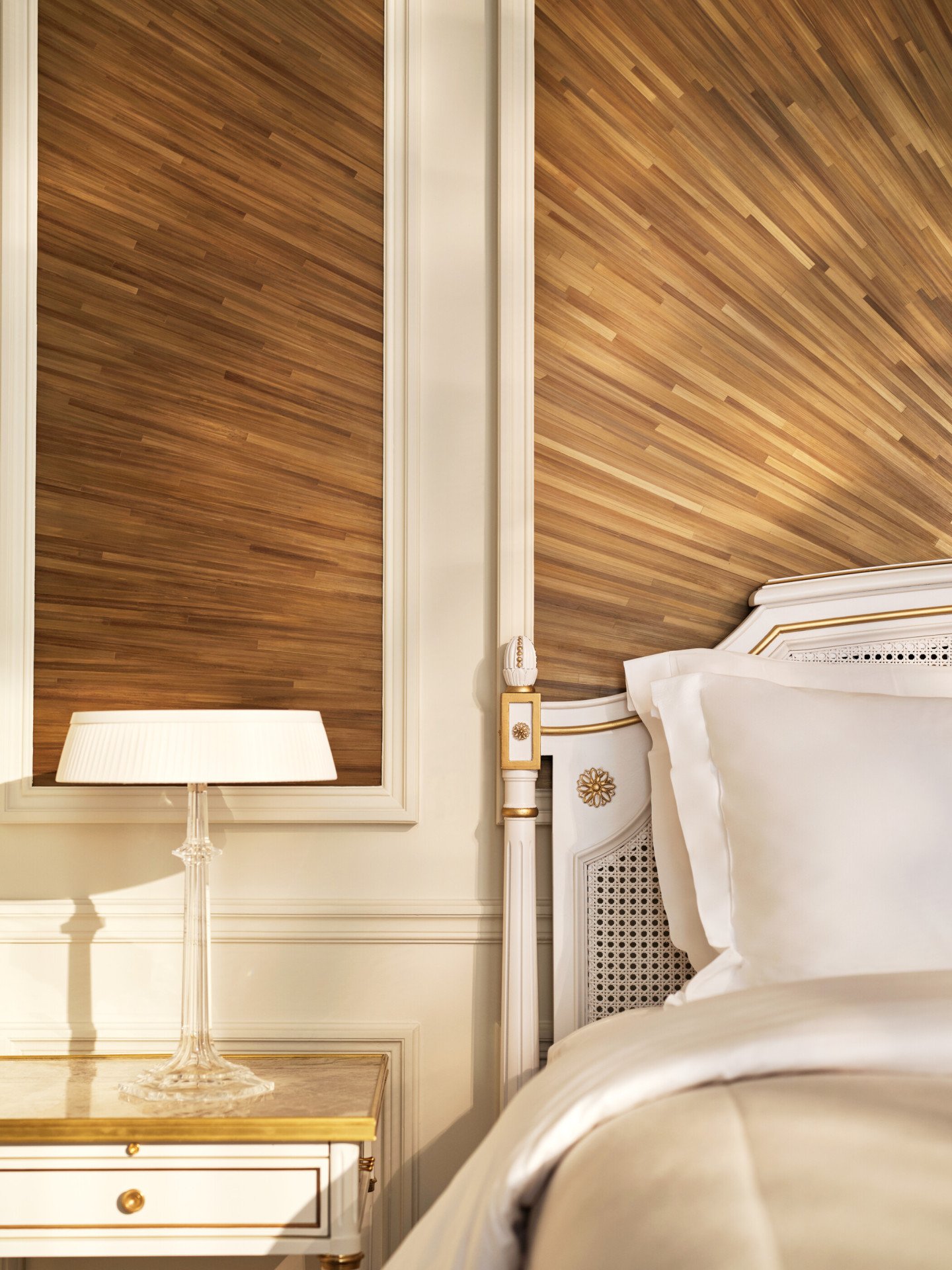 Corner of the right side of the bed, next to a night table and a lamp on the top, and the wall made with straw marquetry, at Le Meurice, Paris
