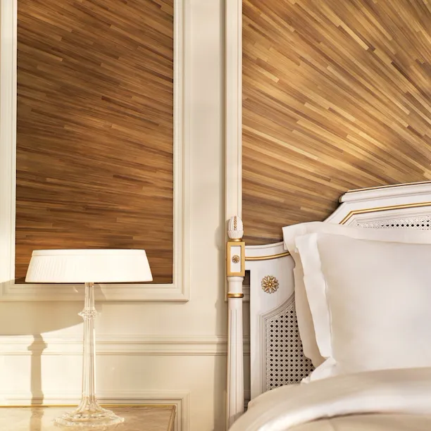 Corner of the right side of the bed, next to a night table and a lamp on the top, and the wall made with straw marquetry, at Le Meurice, Paris