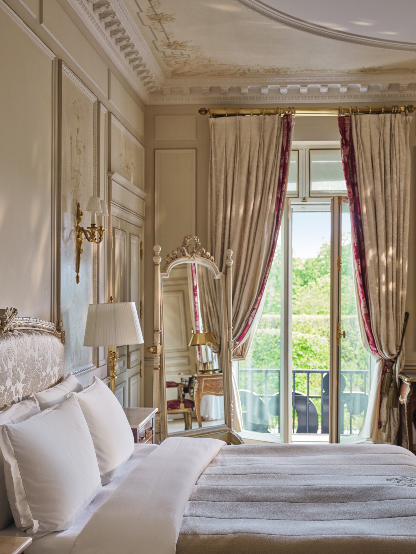 Large view of the right side of the bed with in the background the mirror and the windows and curtains open, at Le Meurice, Paris