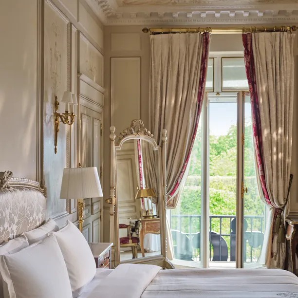 Large view of the right side of the bed with in the background the mirror and the windows and curtains open, at Le Meurice, Paris