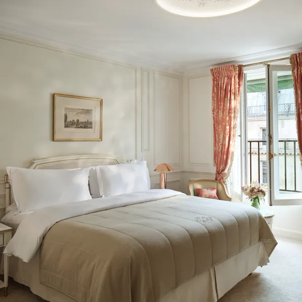 Room of a Pompadour Suite with the bed between two night table and a chair next to a table with flowers on the top, at Le Meurice, Paris