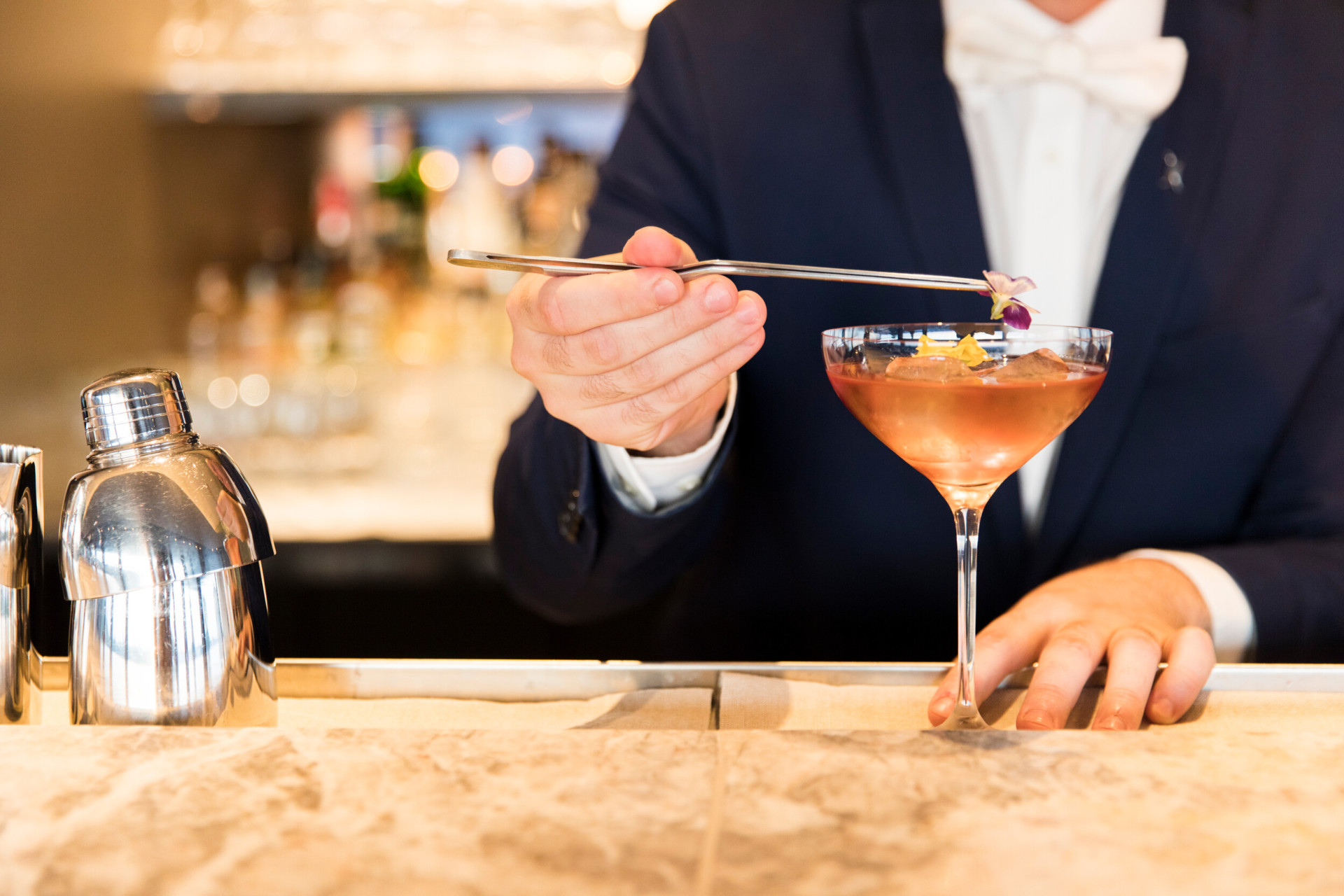 Barman behind the counter adding on top of a cocktail colourful flowers at Il Giardino Bar, Hotel Eden, Roma 