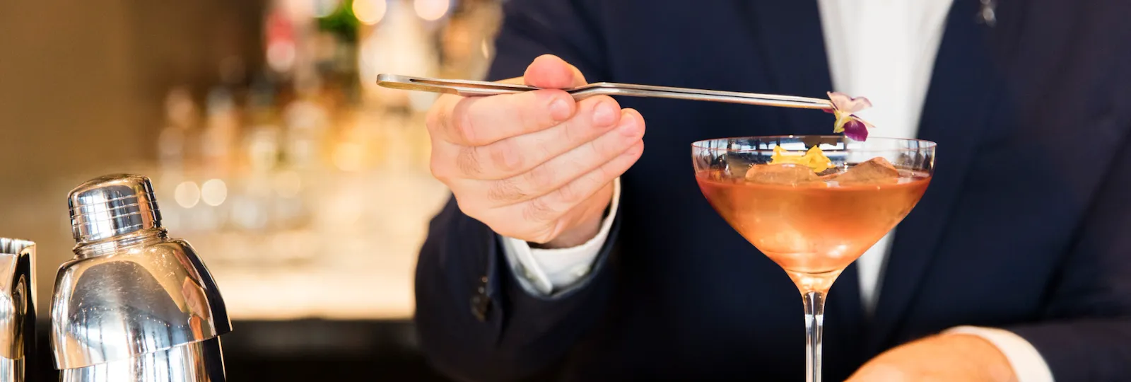Barman behind the counter adding on top of a cocktail colourful flowers at Il Giardino Bar, Hotel Eden, Roma
