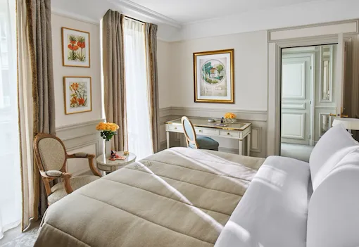 Bedroom in beige and white shades, with queen bed, white wood desk and armchair, at Le Meurice, Paris.
