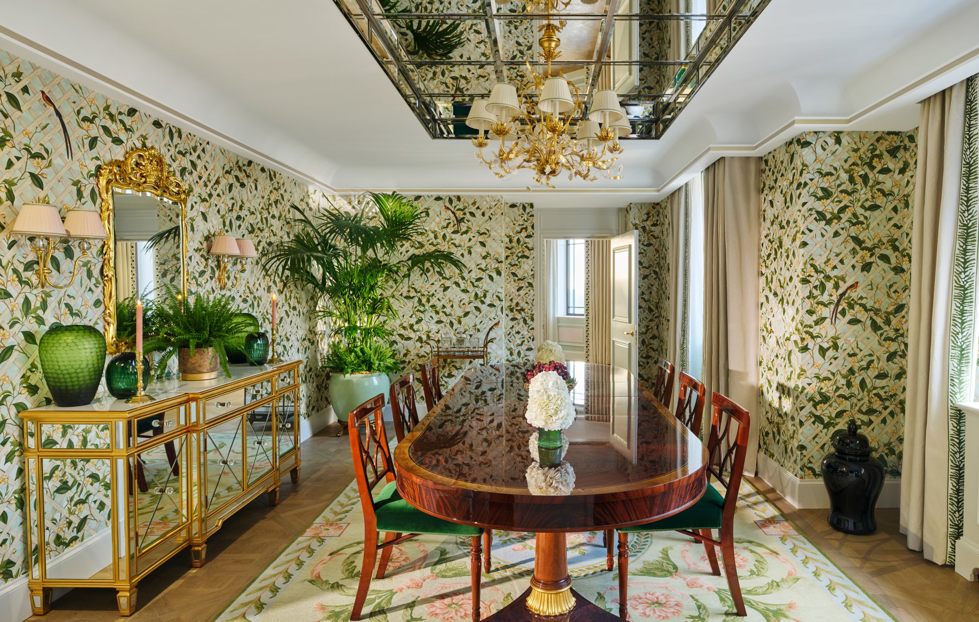 Elegant dining room with floral wallpaper, wooden table, and decorative plants on a sideboard.