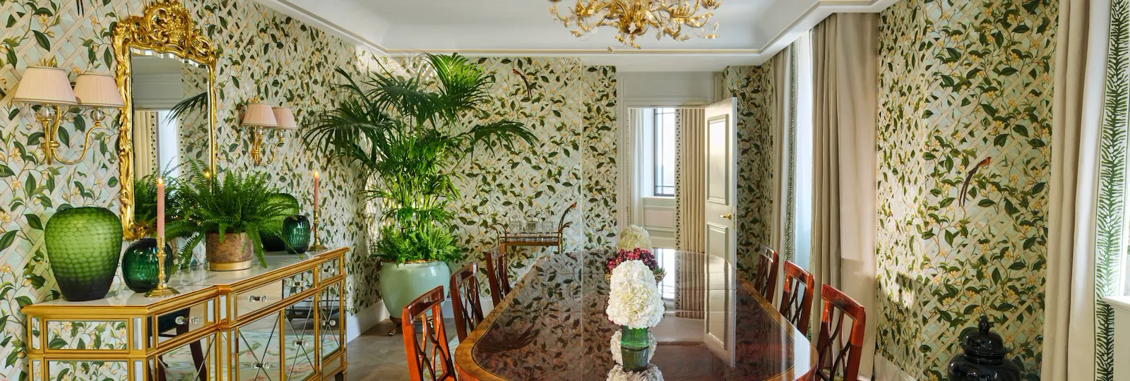 Elegant dining room with floral wallpaper, wooden table, and decorative plants on a sideboard.