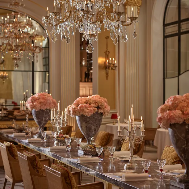 Jean Imbert au Plaza Athénée's central marble table, drawned up with pink flowers and chandeliers. Crystal chandelier hanging above the table. At Hotel Plaza Athénée, Paris