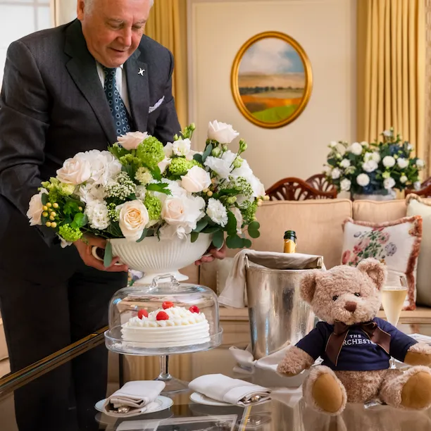 Butler in Dorchester suite with floral arrangement, champagne and Dorchester teddy bear