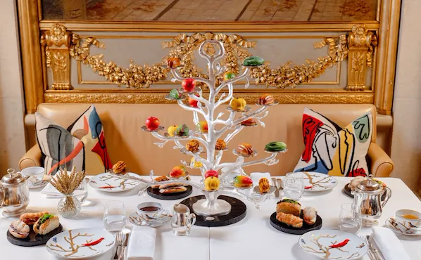Festive table with a white Christmas tree, plates, glasses, and colorful artwork cushions.