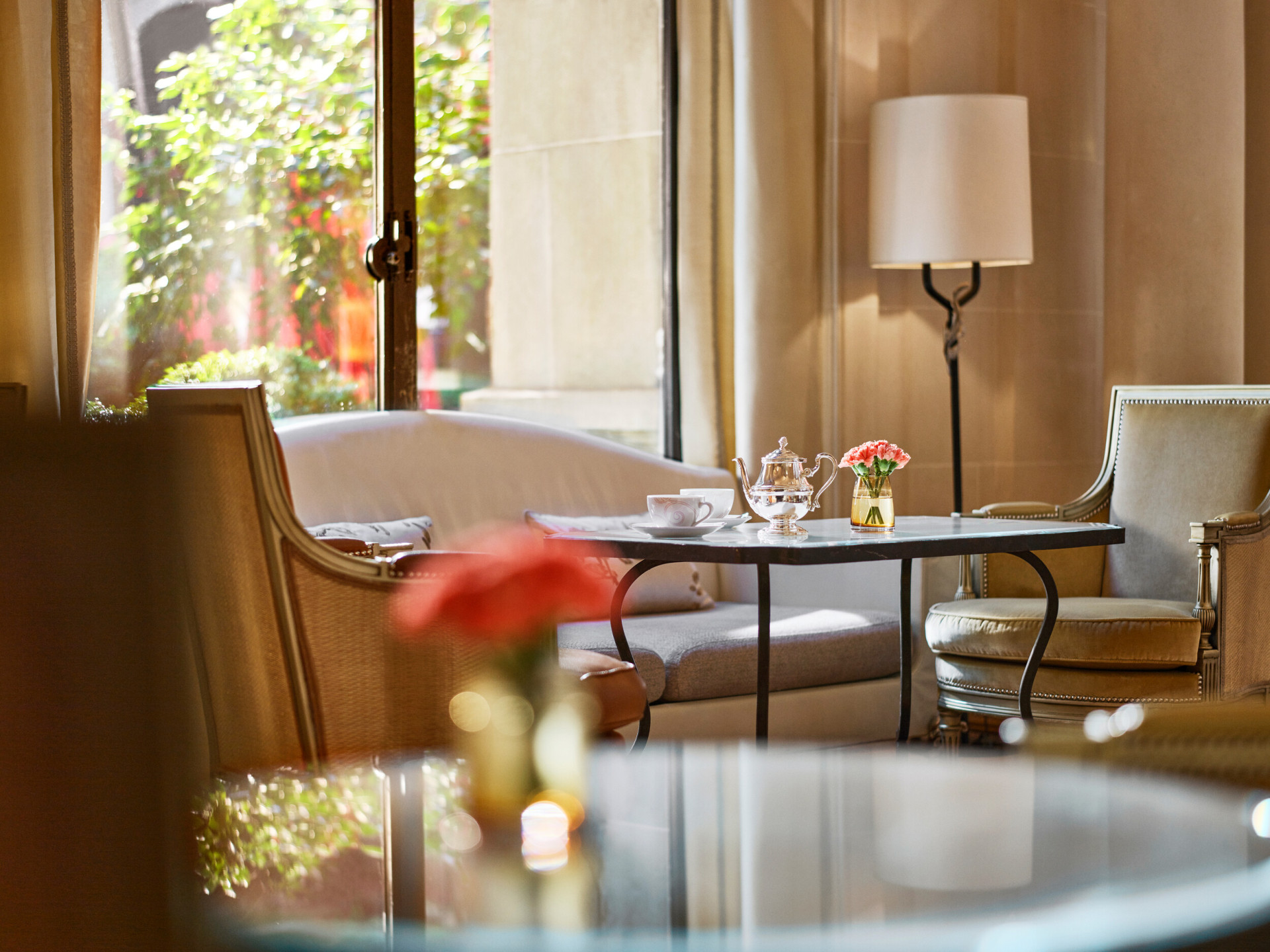 Close up of a dining table at la galerie, table with cups of tea, two armchairs and a sofa next to a sunny window, at Hotel Plaza Athénée, Paris