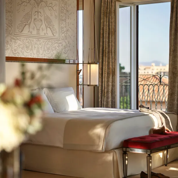 Elegant bedroom Presidential Suite, headboard with peacocks decoration and big window with view of Rome at Hotel Eden