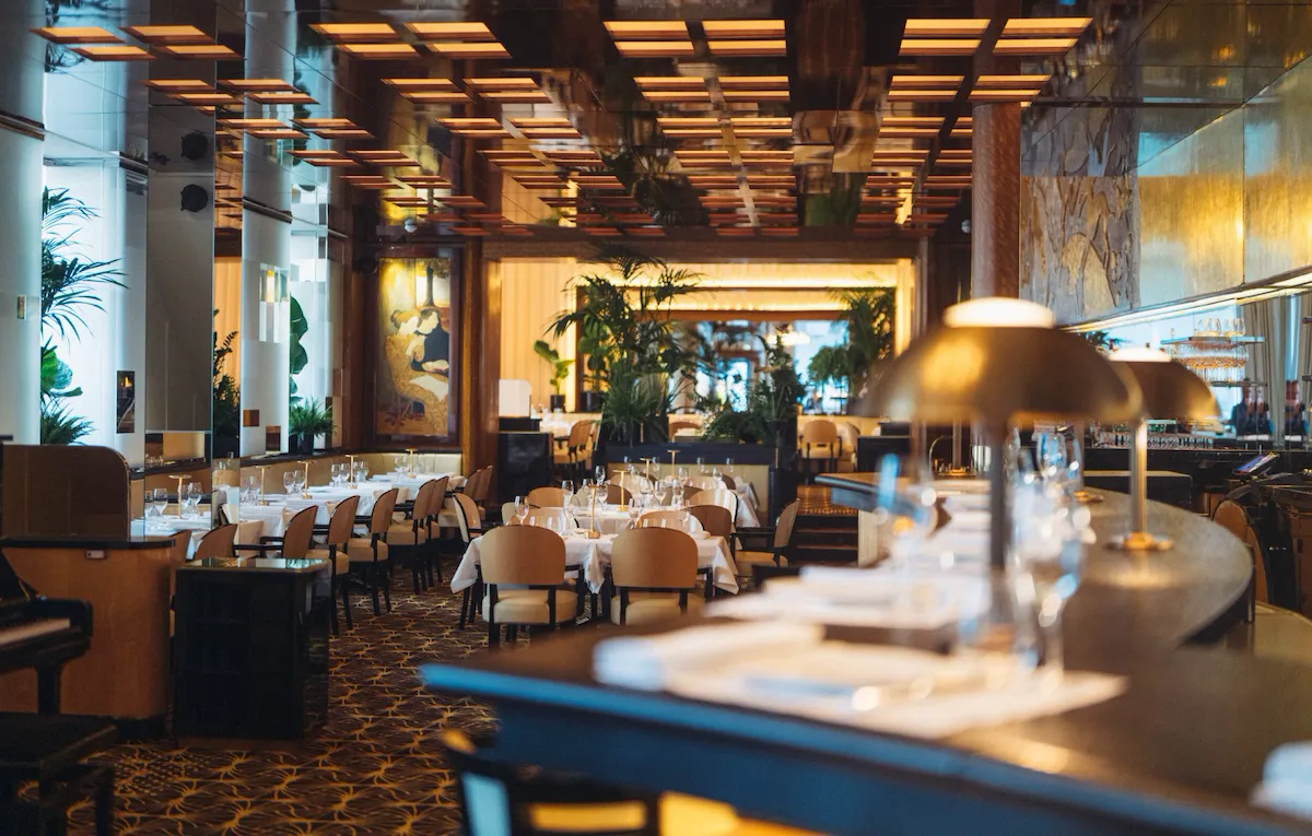 Overview of Le Relais Plaza's dining room lower deck, with the bar at the forefront,at Hotel Plaza Athénée, Paris