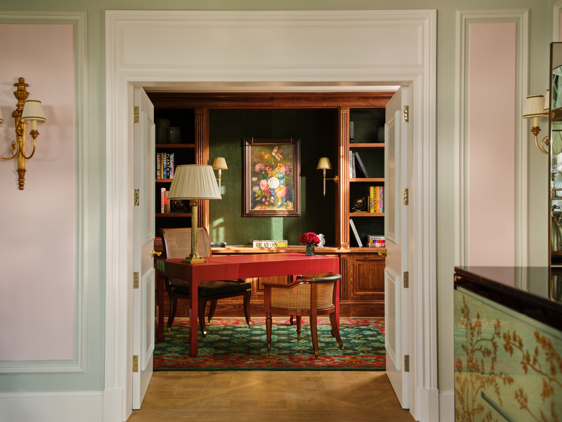 A formal room with a desk, chairs, shelves, artwork, and warm lighting creating a cozy atmosphere