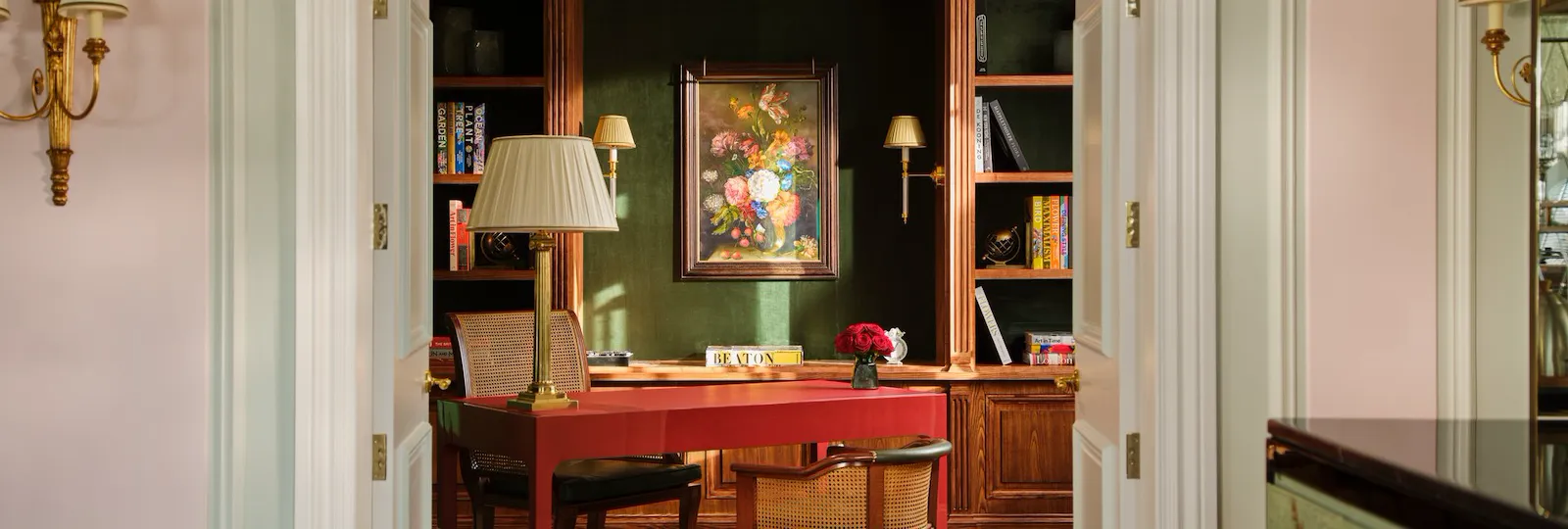 A formal room with a desk, chairs, shelves, artwork, and warm lighting creating a cozy atmosphere