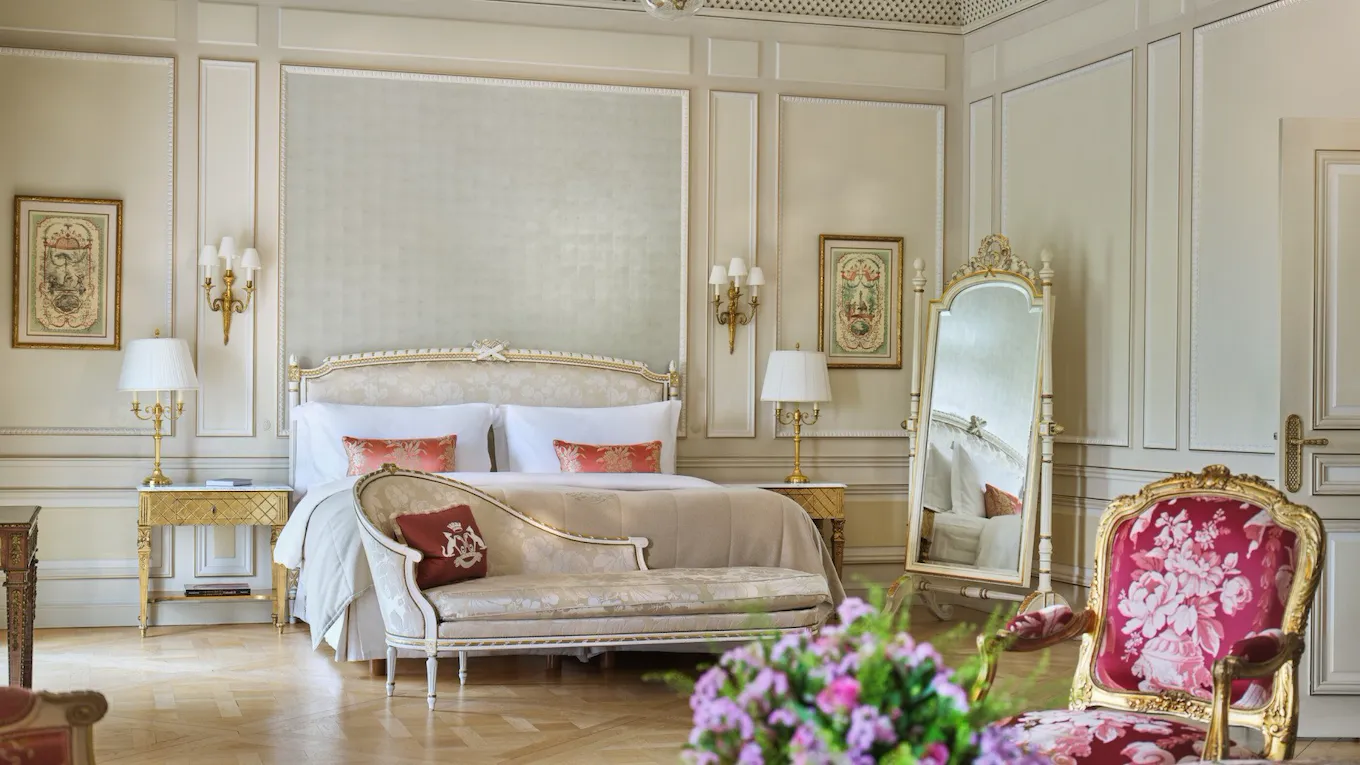 Large view of a Versailles suite with on the foreground a bouquet of flowers and chairs, and behind a couch close to the bed, at Le Meurice, Paris