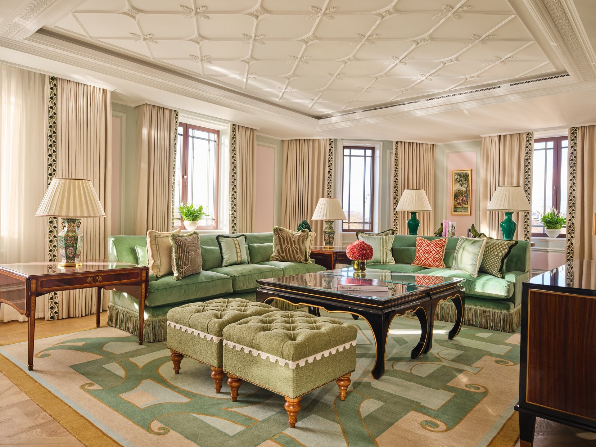 Elegant living room with green sofas, lamps, windows, and decorative rugs creating a cozy atmosphere