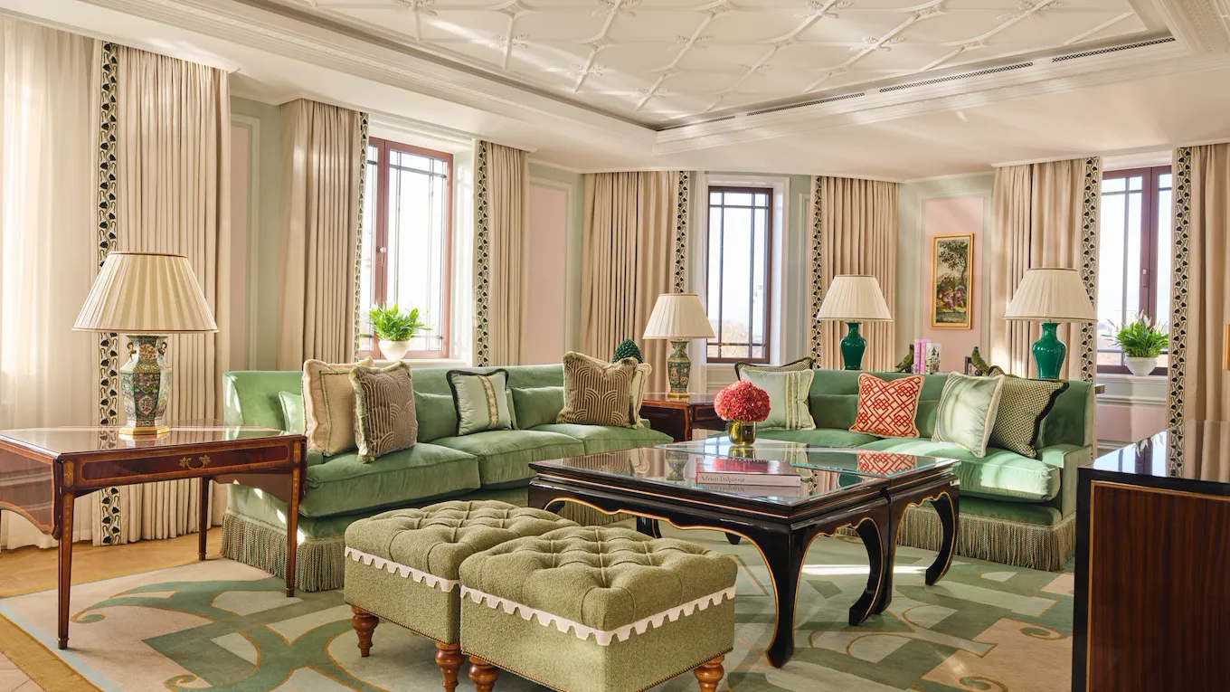 Elegant living room with green sofas, lamps, windows, and decorative rugs creating a cozy atmosphere