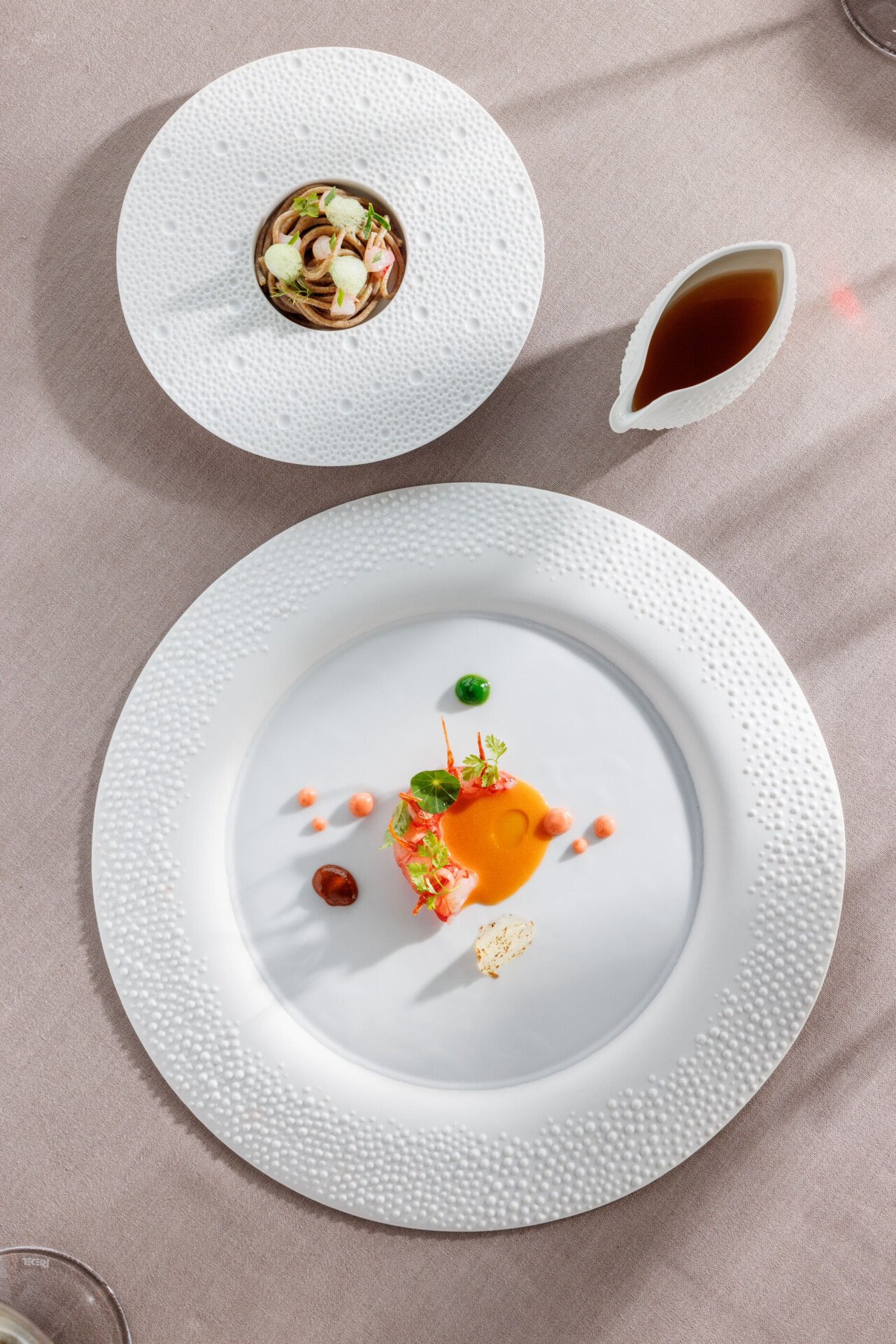 Two round tables laid ona  table one with a langoustine on a sauce and the other with ramen in it, next a bowl with ramen broth