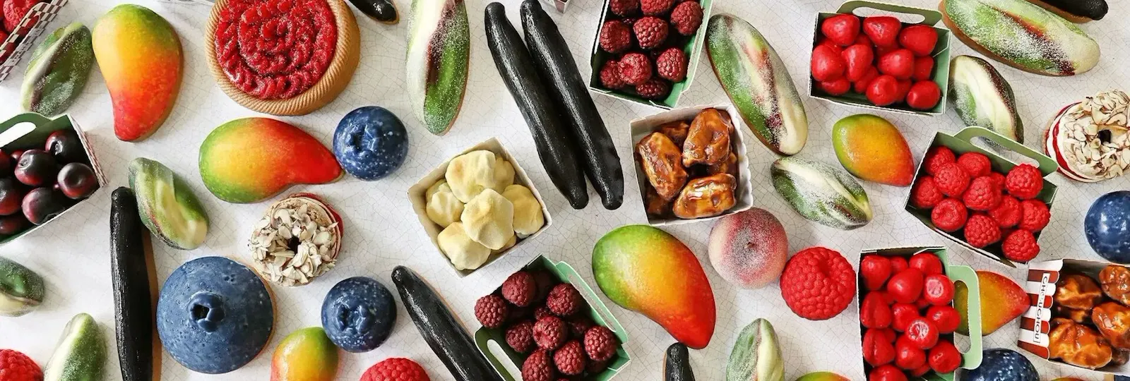 Three green cartons filled with various trompe l'oeil red and dark berries, including raspberries, strawberries, and blackberries, on a light background. At Le Meurice, Paris.