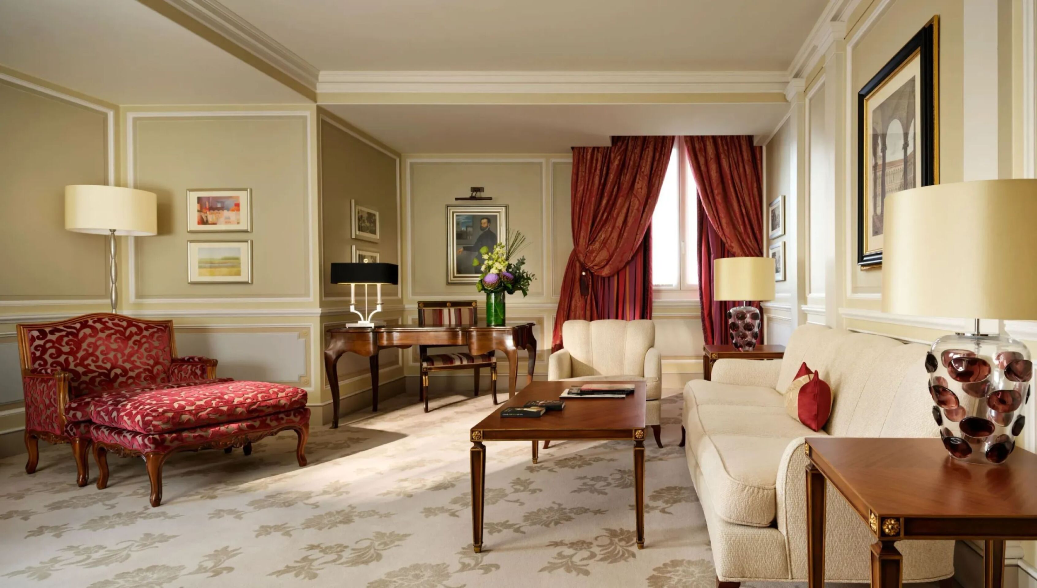 Principe Suite living room with red elements and a bouquet of flowers on the desk in the background 