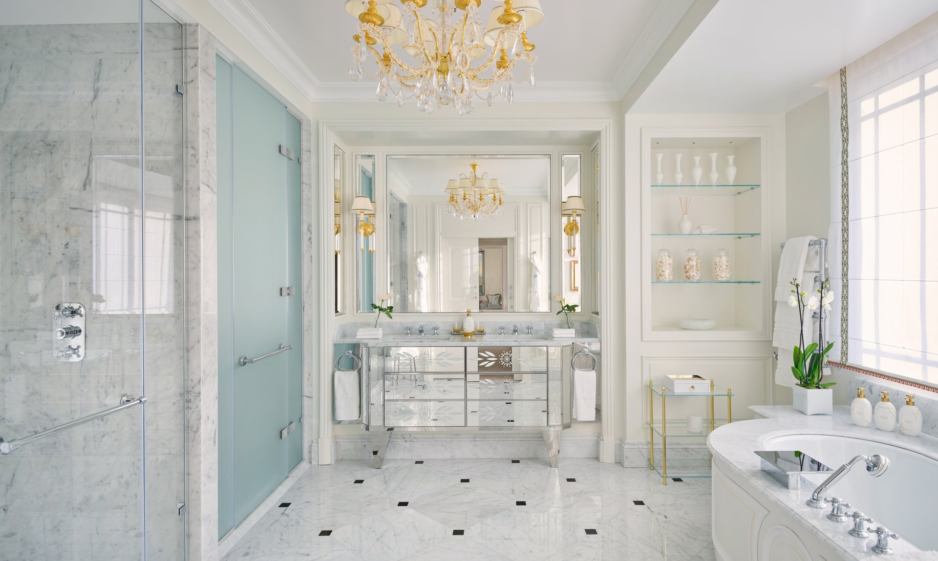 Luxurious bright bathroom with chandelier, marble surfaces, and elegant decor.