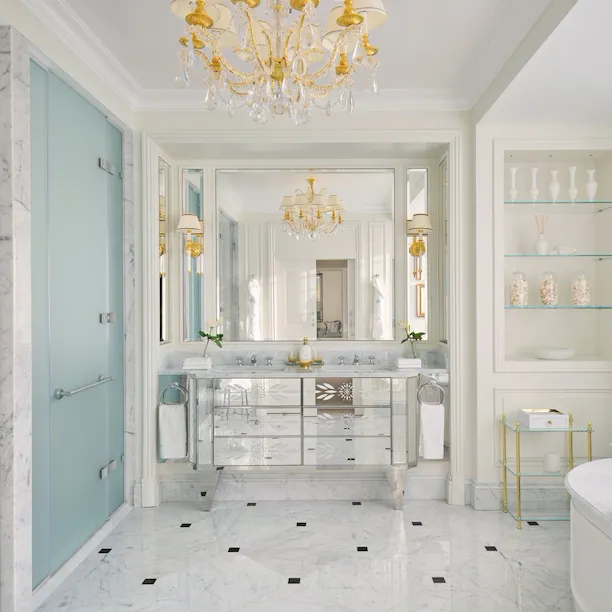 Luxurious bright bathroom with chandelier, marble surfaces, and elegant decor.