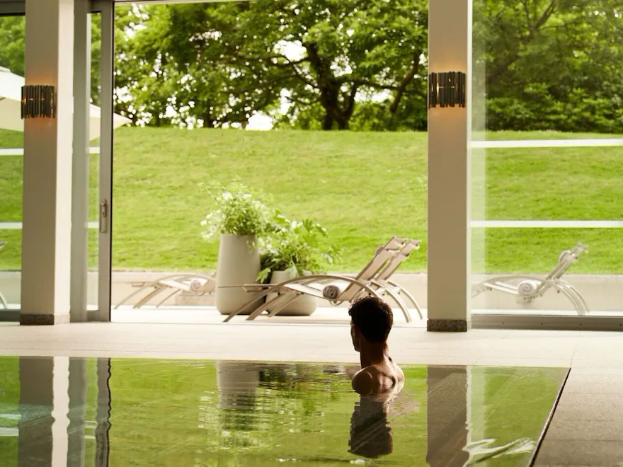 Guests enjoying the pool at Coworth Park with beautfiul light flooding through the open doors to the lush green forest and hills