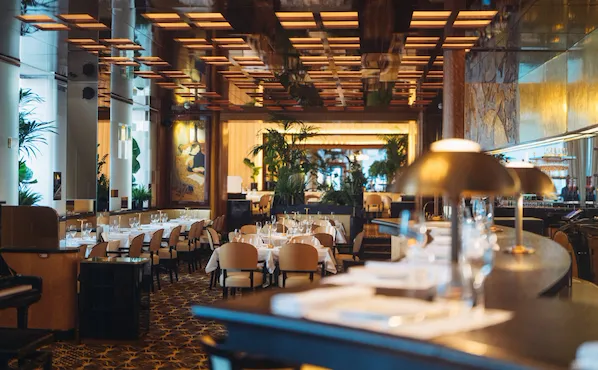 Overview of Le Relais Plaza's dining room lower deck, with the bar at the forefront,at Hotel Plaza Athénée, Paris
