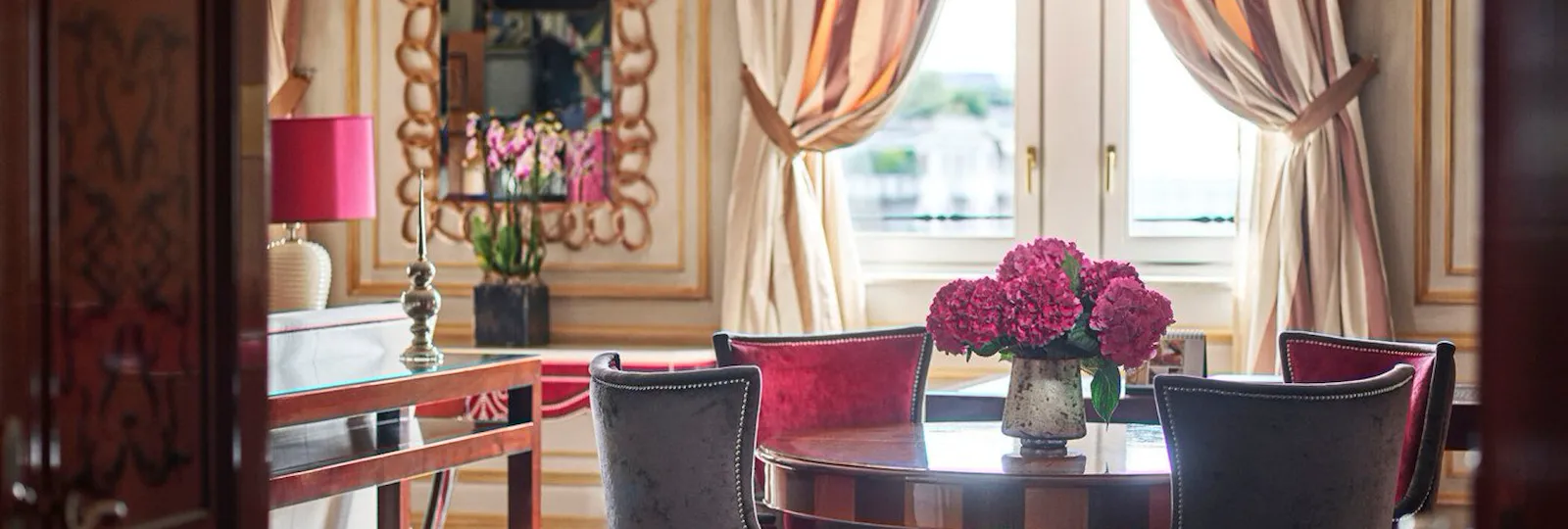 Executive Suite Living Room furnished with a wooden table, four red velvet chairs and a bouquet of pink flowers