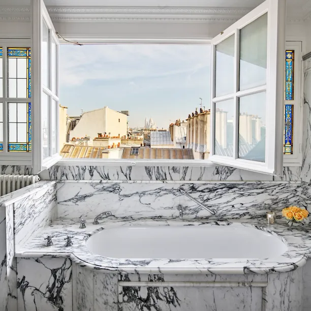 Marble bathroom with open windows overlooking roofs of Paris in an executive junior suite at Le Meurice, Paris.