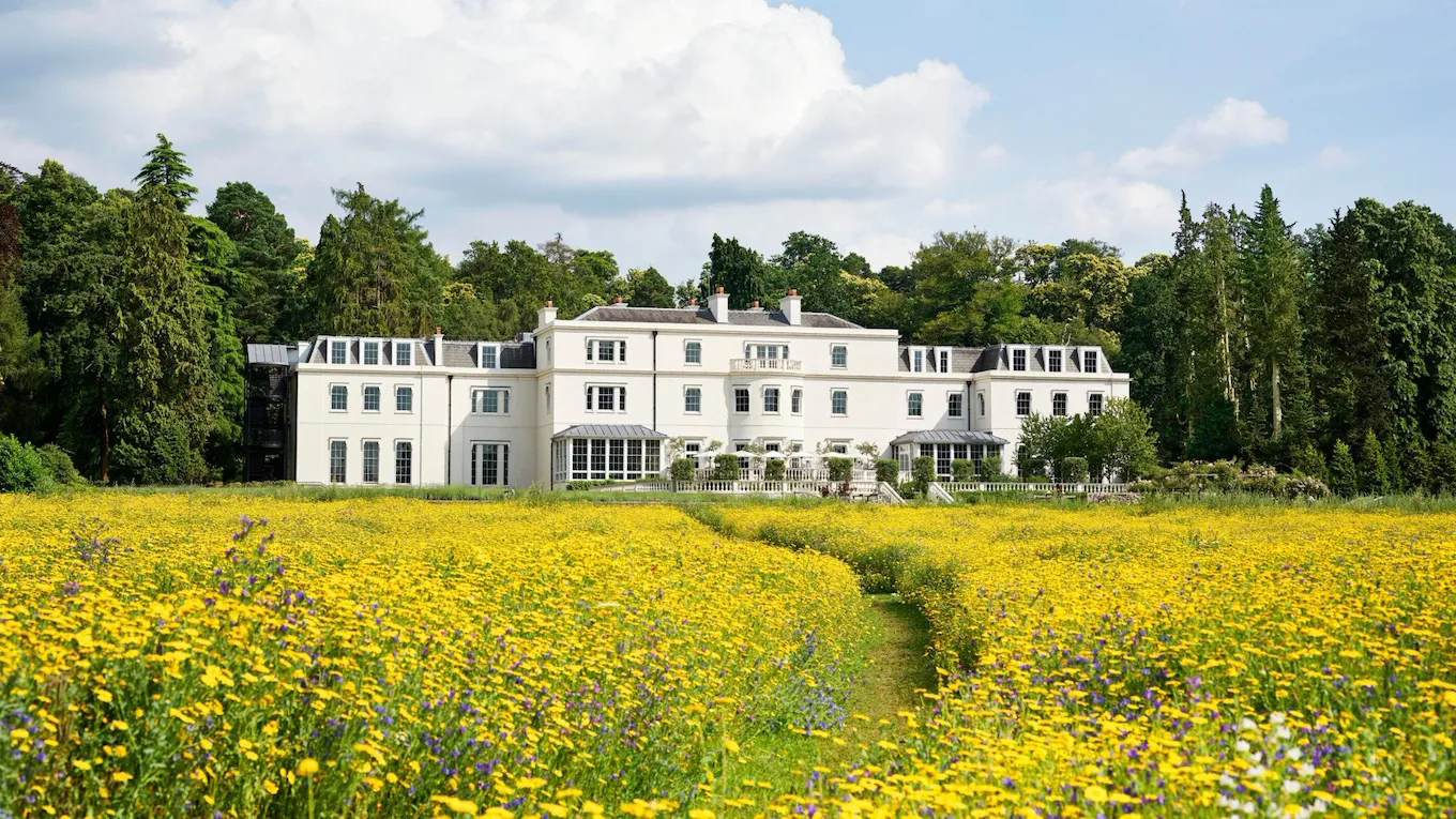 Exterior facade of Coworth Park with yellow wildflower meadow in front, Ascot