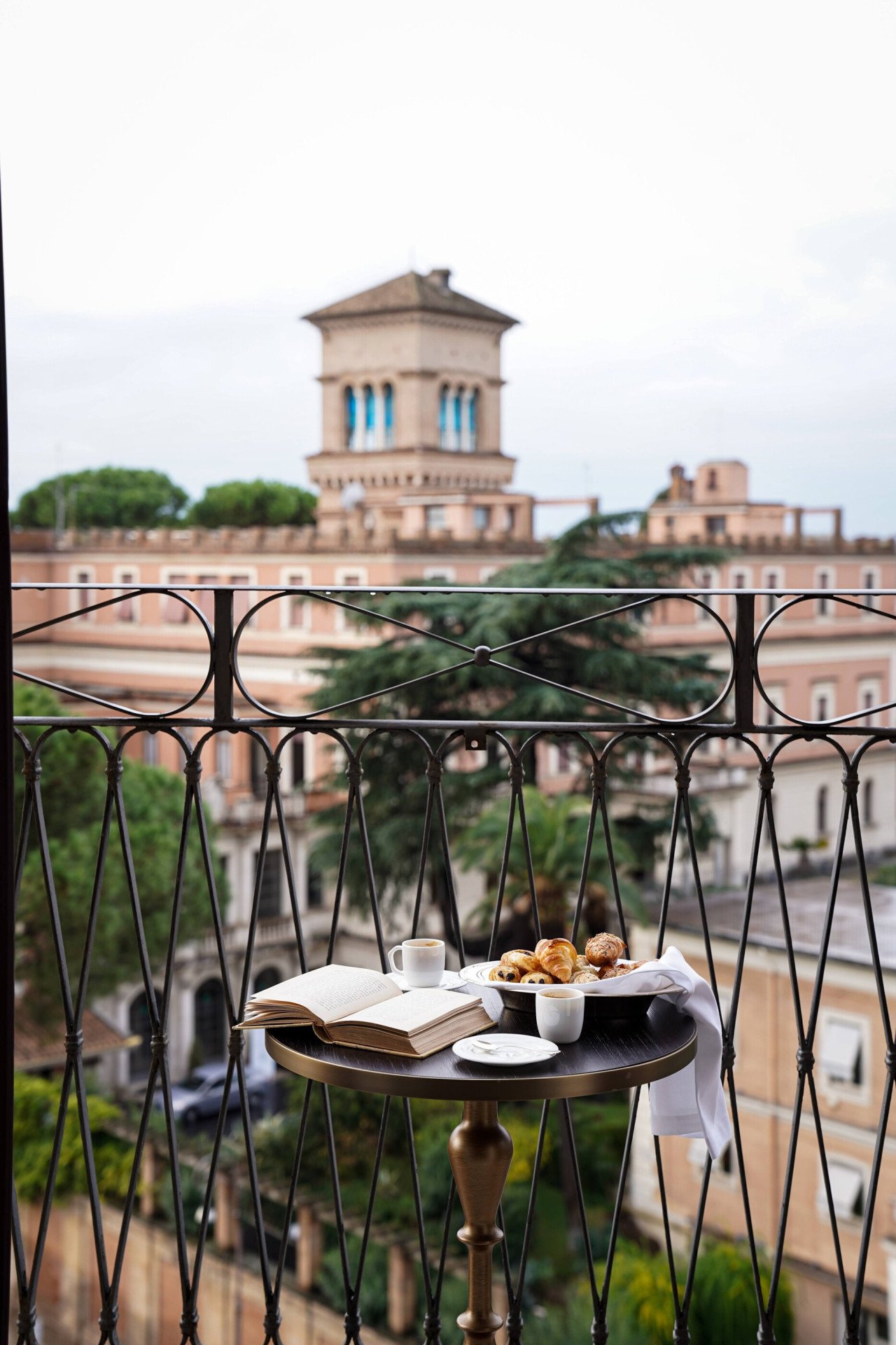 Smal round table set on a balcony facing Rome laid with due coffee cups and pastries ina  basket