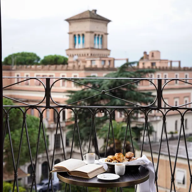 Smal round table set on a balcony facing Rome laid with due coffee cups and pastries ina basket