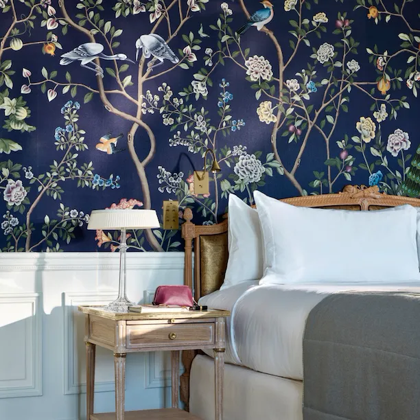 Portrait shot of the bedside table in an executive room, with a pouch and a book placed on the table. The bed highlights the dark blue hand painted wall. At Le Meurice, Paris.