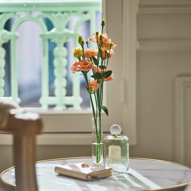 Flowers, a bottle of perfume and a clutch placed on a low marble table in a superior room. At Le Meurice, Paris.