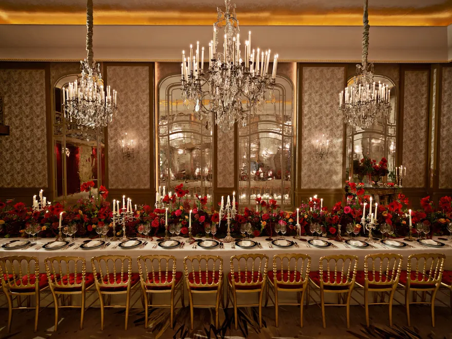 Dinner set up with a long table and red flowers captured in Le Salon Haute Couture, at Hôtel Plaza Athénée, Paris - Dorchester Collection.