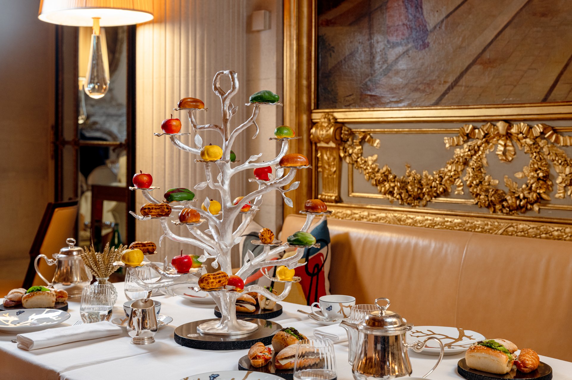 Elegant dining table set with a colorful decorative tree in a luxurious, warmly lit room