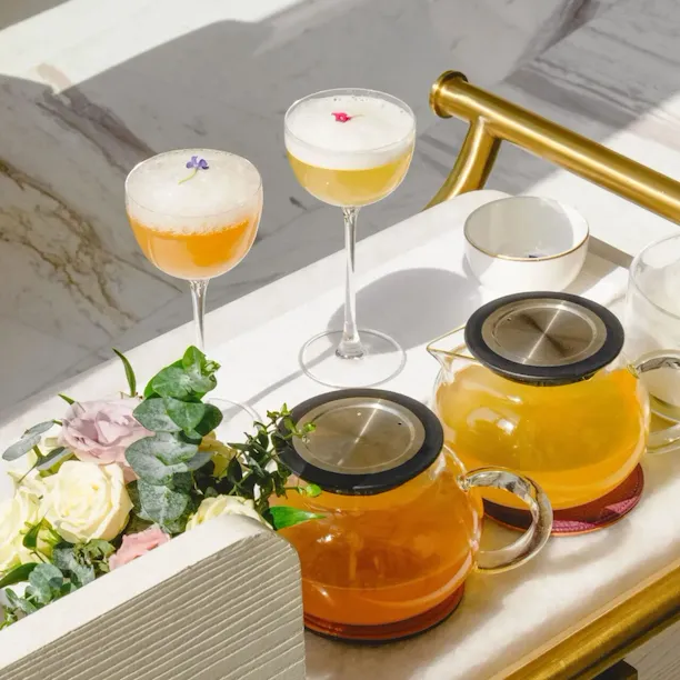 Summer Afternoon Tea at The Gallery located at The Lana, Dorchester Collection, Dubai. Including bites and beverage offerings. The afternoon tea is served in the lobby, on a table dressed with a white cloth against soft shadows.