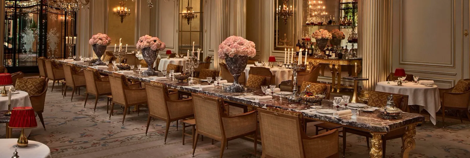 Overview of the Jean Imbert au Plaza Athénée Dining Room and its central marble table with flowers and crystal chandeliers hanging from the ceiling. At Hotel Plaza Athénée, Paris