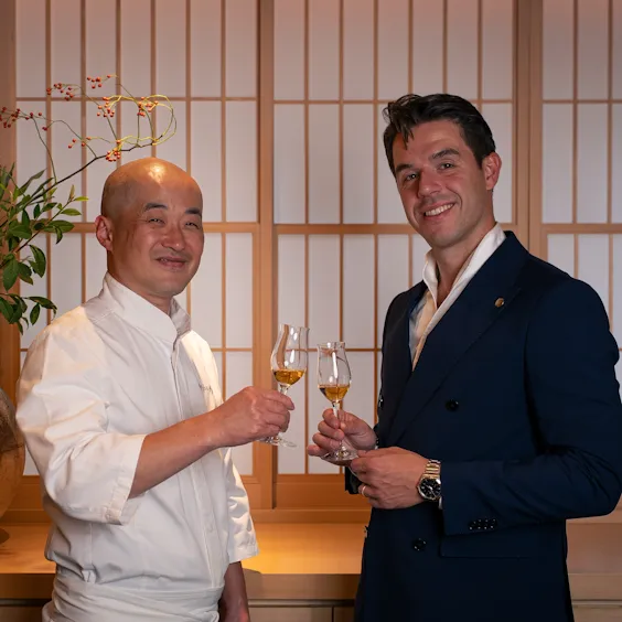 2 people standing in omakase restaurant holding glasses of whisky to promote collaboration dinner