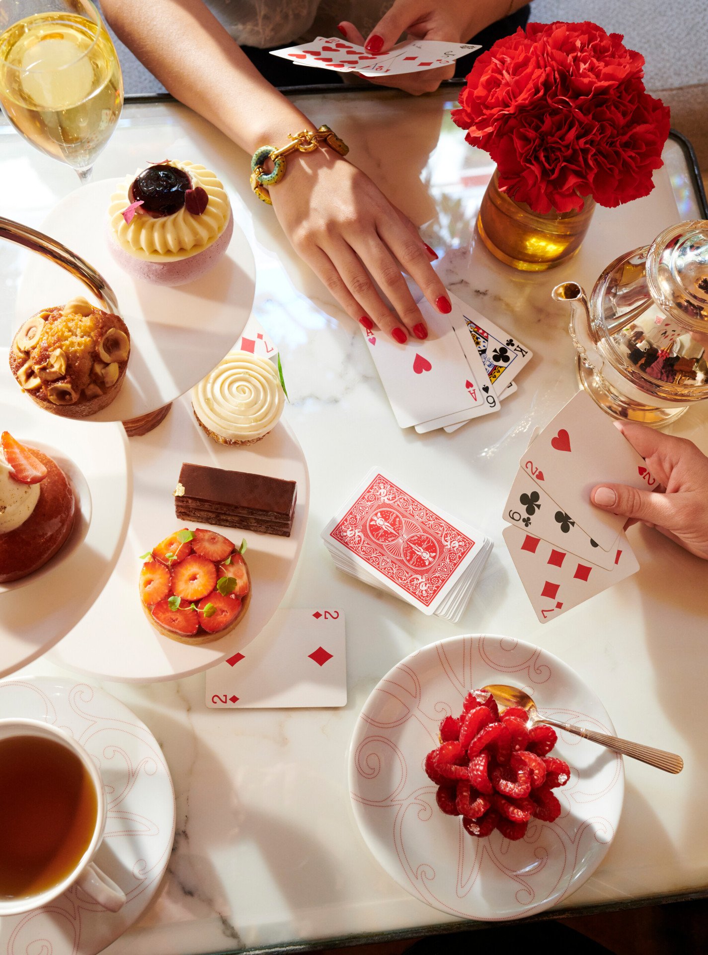 Two hands playing cards on a table dressed with a tea time at La Galerie, Plaza Athénée. 