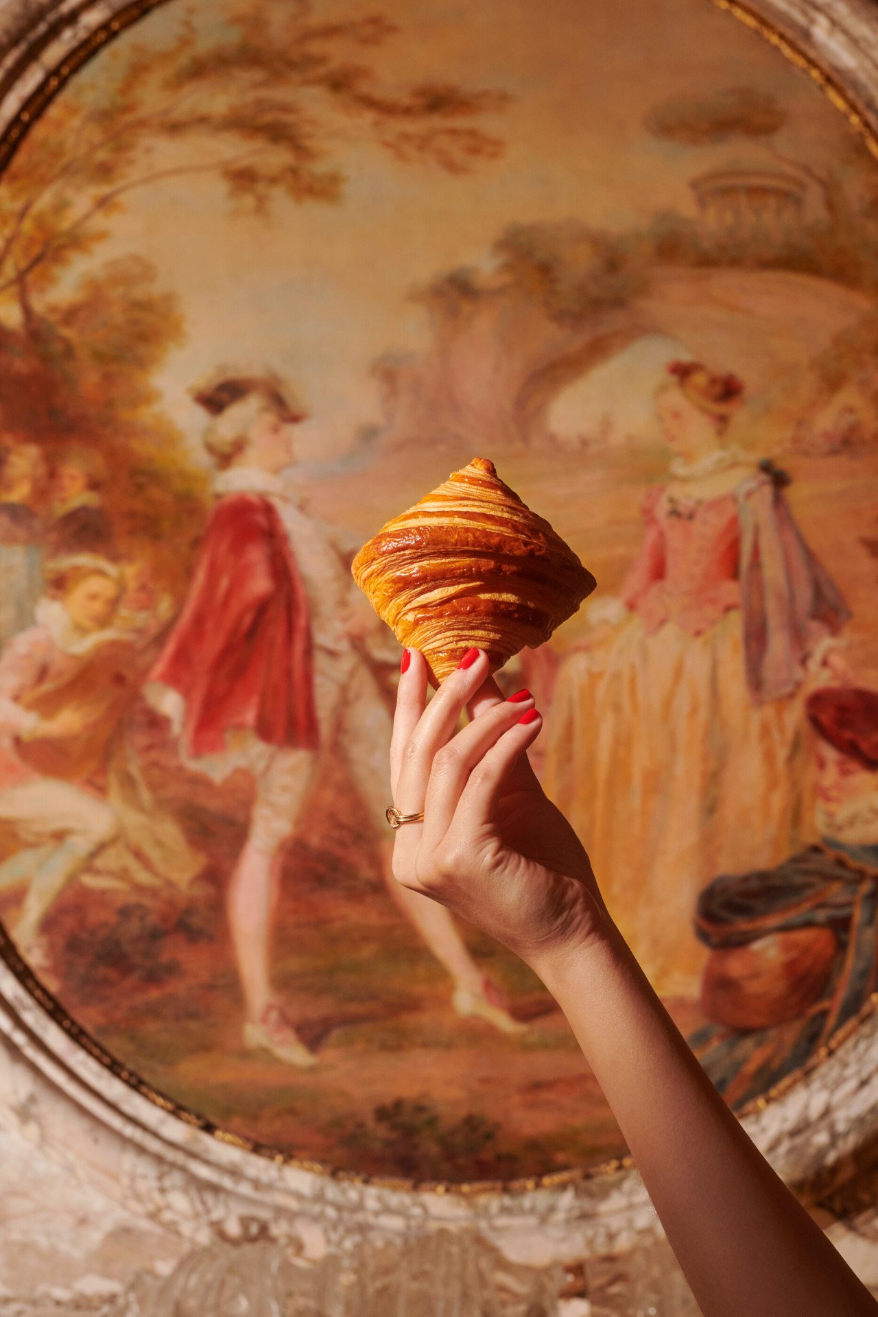 Hand holding a croissant in front of a painting at Le Meurice, Paris - Dorchester Collection