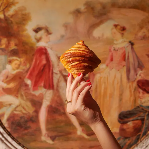 Hand holding a croissant in front of a painting at Le Meurice, Paris - Dorchester Collection