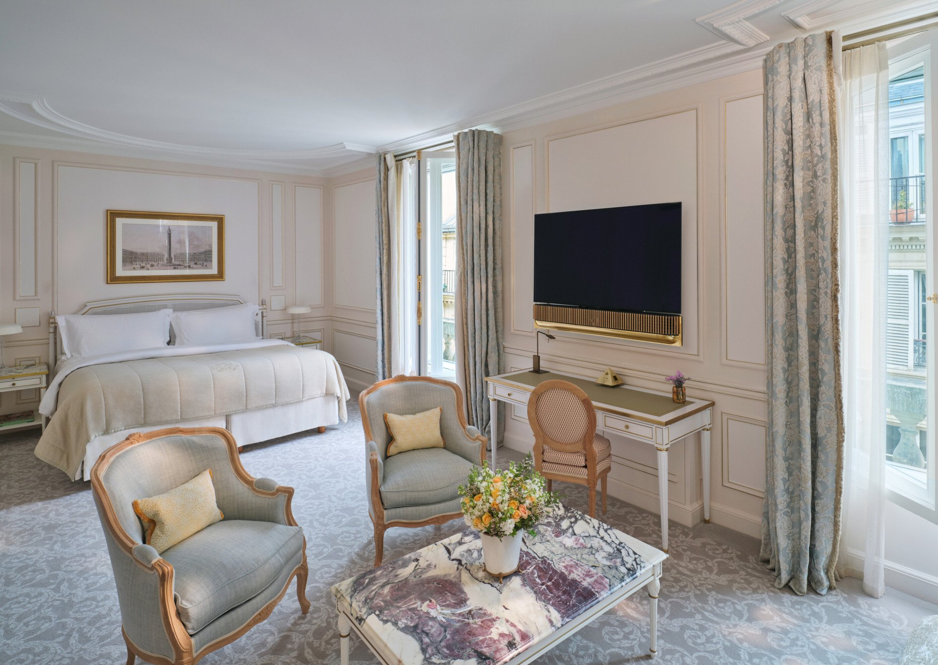 Large view of a Deluxe Junior Suite with the stone marquetry on the table and the TV and the Bed on the background, at Le Meurice, Paris