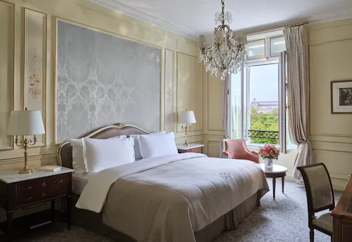 Heritage Suite view from the right side of the bed, next to a chair and a table with flower on the top, in front of the window, at Le Meurice, Paris